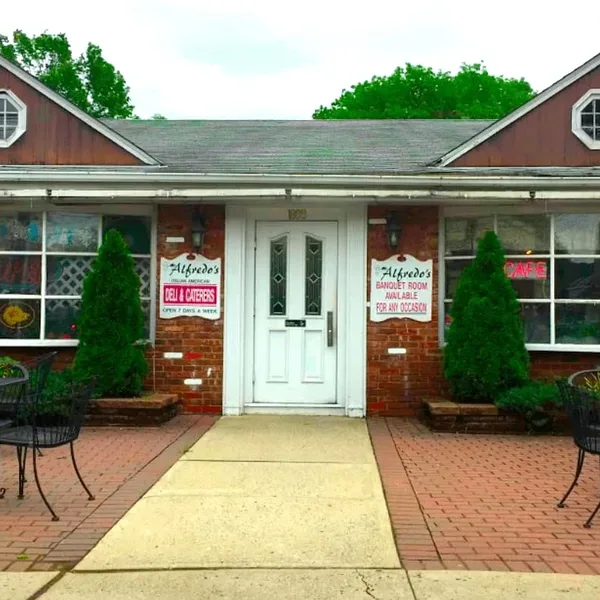 The brick storefront with its white door, deli and banquet room signs, and patio tables on either side